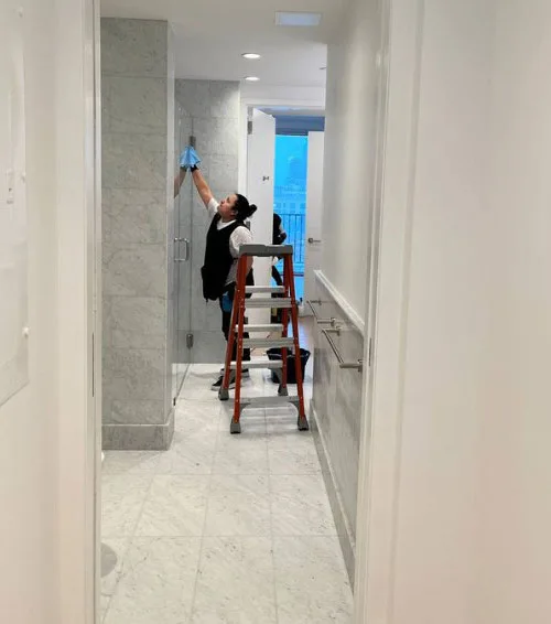 Cleaner on a ladder wiping high glass surfaces — high dusting services in Temecula, CA