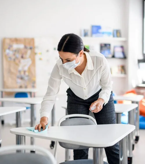 Cleaner disinfecting a classroom desk